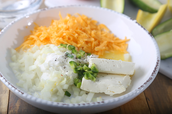 Shredded cheddar, cream cheese, diced onion, and jalapeno in a white bowl