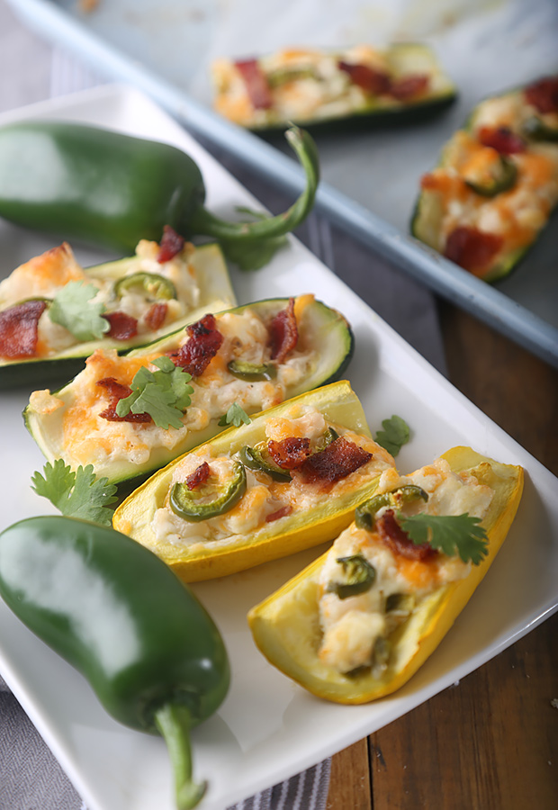 Baked twice-baked zucchini boats with bubbling cheddar, bacon, and jalapeno on a white platter