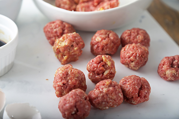 Raw ground beef meatballs shaped by tablespoon lined up on a board