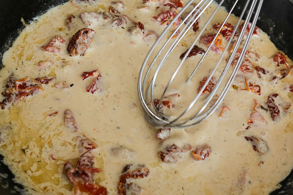 Adding cream to the sun-dried tomato sauce.