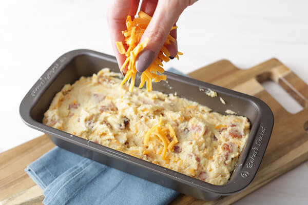 Bread batter in a loaf pan with cheese being sprinkled on top.