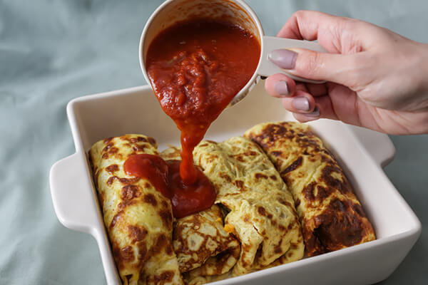 Pouring enchilada sauce on top.