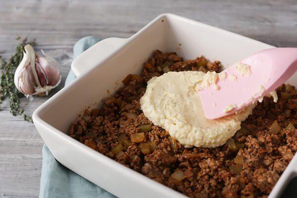 Spreading mash cauliflower on casserole.