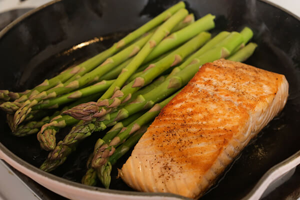 Salmon and asparagus cooking in a pan.