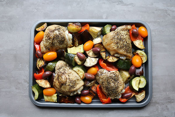 Adding the tomatoes to the baking sheet with the Greek chicken.