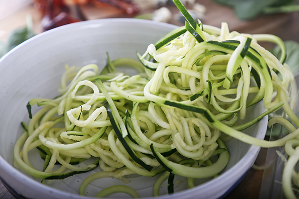 Spiralized zucchini noodles piled high in a white bowl with green skin strips visible