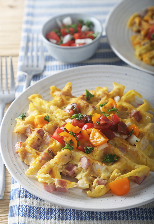 Plated chicken, ham, and Swiss waffle topped with halved cherry tomatoes and fresh parsley