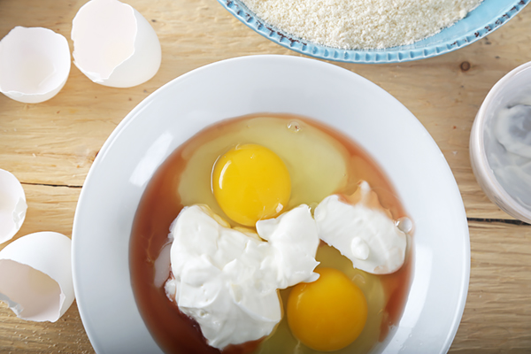 A pair of cracked eggs and sour cream in a white bowl with red wine vinegar