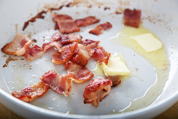 Chopped bacon crisping in a skillet with a pat of butter melting alongside
