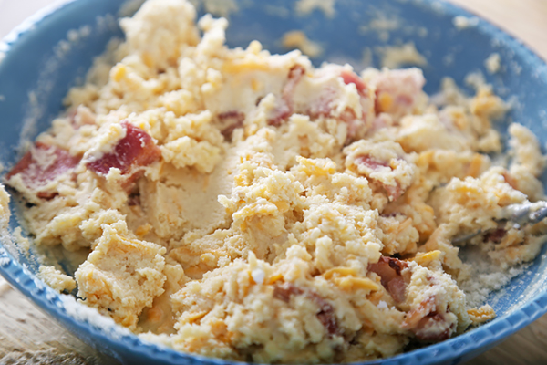 Thick muffin batter with bacon pieces and cheddar stirred together in a blue bowl