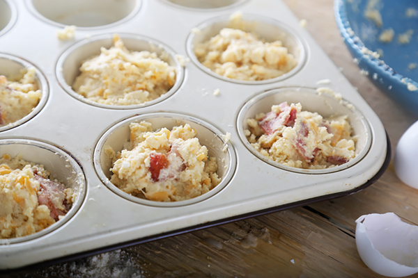Bacon cheddar muffin batter spooned into a greased metal muffin tin