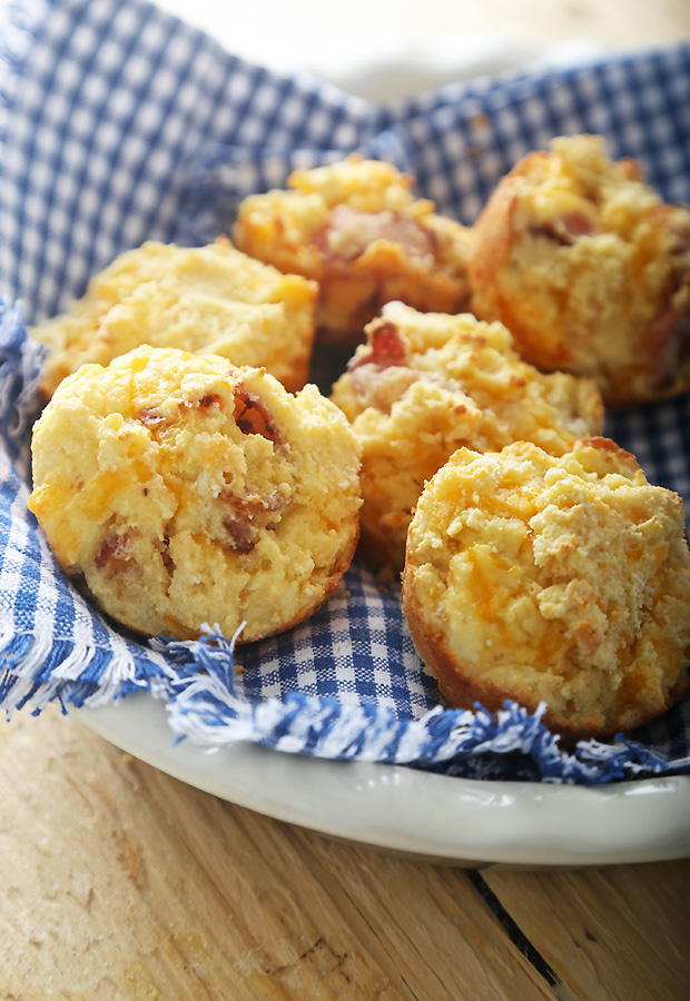 Golden baked bacon and sour cream muffins piled on a plate with a blue checkered napkin