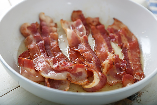 Bacon strips frying until browned and curled in a white skillet