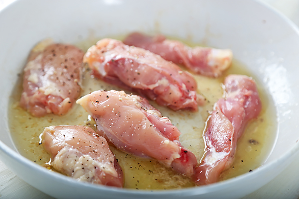 Seasoned chicken thighs frying in bacon grease and butter in a skillet