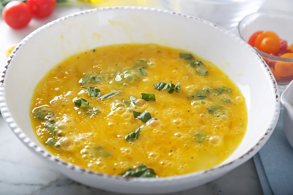 Beaten eggs with torn basil leaves and black pepper in a ceramic bowl