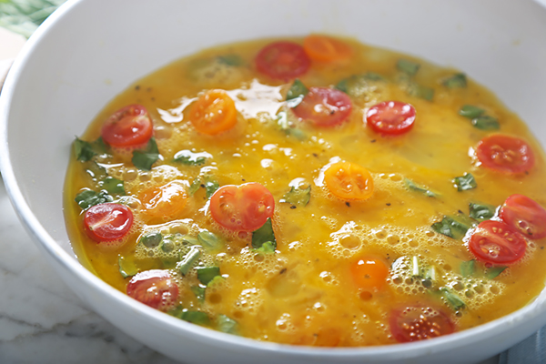 Egg mixture poured over cherry tomatoes with basil, setting in the pan
