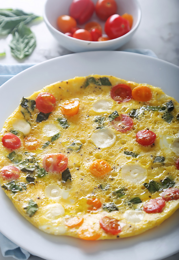 Caprese omelet with melted mozzarella, cherry tomatoes, and basil cooked flat on a plate