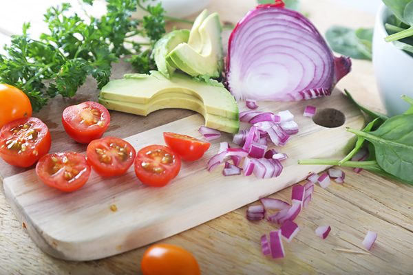 Halved cherry tomatoes, sliced avocado, and diced red onion on a wooden prep board