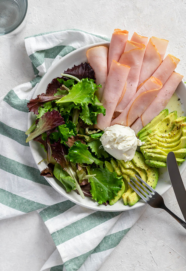 Seasoned keto turkey plate with sliced avocado, spring mix, and cream cheese beside a fork