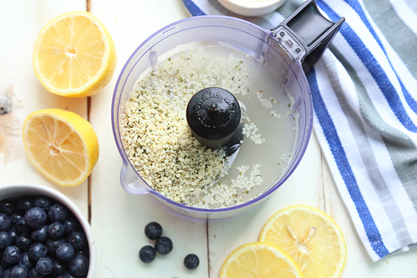 Hemp seeds and hot water in a blender with halved lemons and blueberries beside it