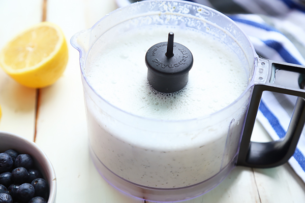 Blended hemp seed yogurt with frothy surface in a food processor beside lemon and blueberries