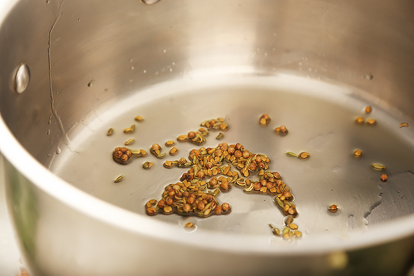 Cumin, coriander, and fenugreek seeds toasting in olive oil in a stainless steel pot