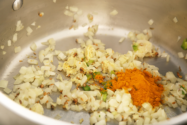 Chopped onion sauteing with ginger, garlic, turmeric, and chopped jalapeno in a steel pot