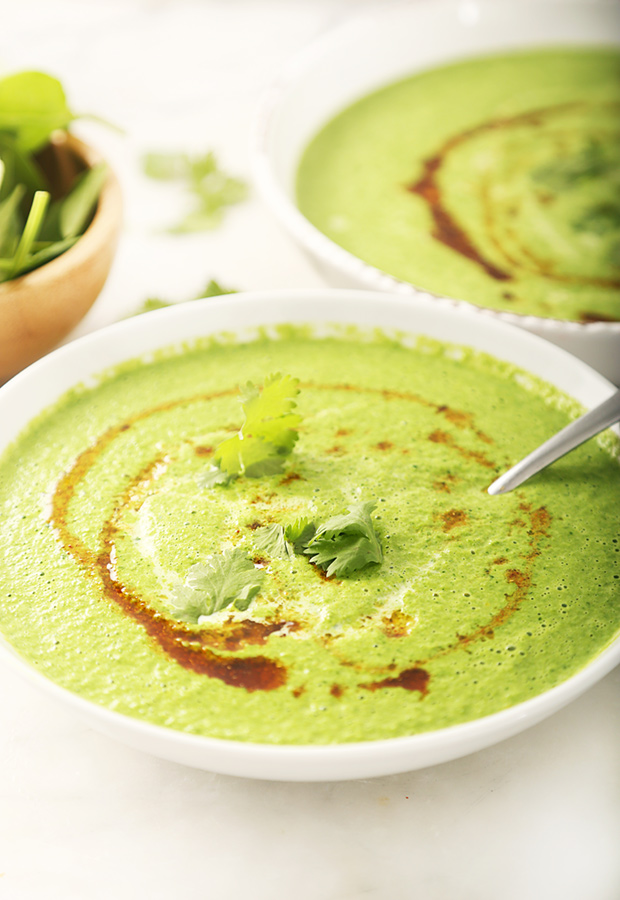 Smooth blended green soup with a paprika ghee drizzle and cilantro in a deep bowl