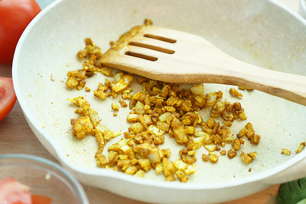 Diced onion and garlic browning with curry and turmeric in a white skillet