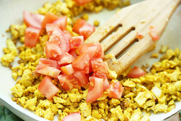 Diced fresh tomatoes added on top of turmeric-seasoned crumbled tofu in a skillet
