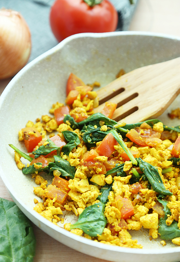Curried tofu scramble with wilted spinach and softened tomatoes in the pan