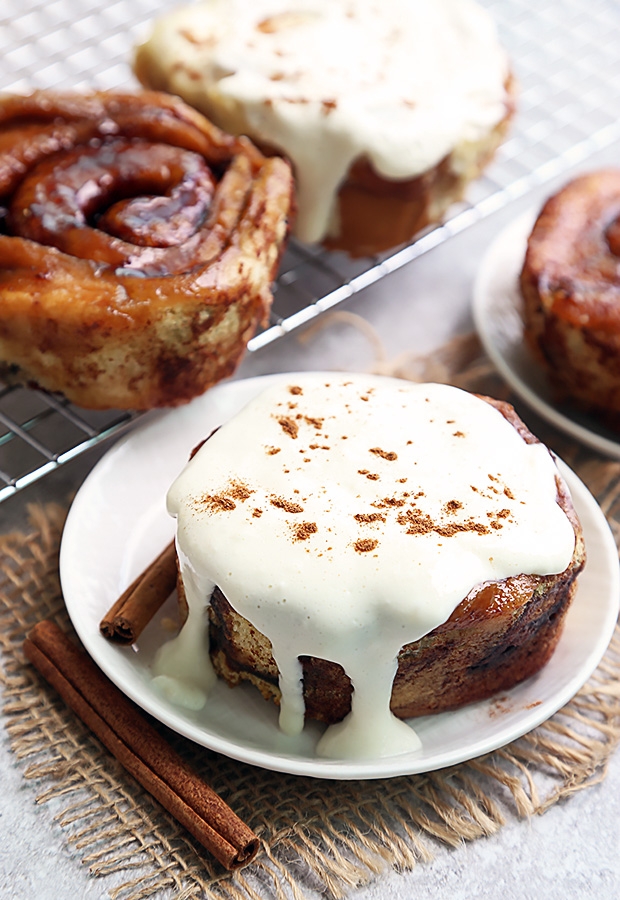 Cinnamon roll mug cakes with thick cream cheese frosting and cinnamon dust on a plate