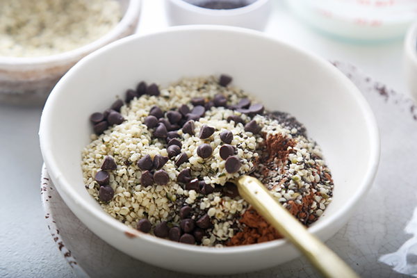 Hemp hearts, dark chocolate chips, cocoa powder, and chia seeds in a white bowl before stirring