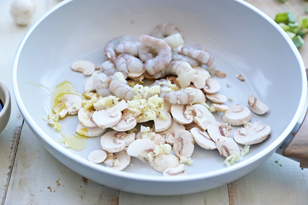 Raw shrimp, sliced button mushrooms, and minced garlic in avocado oil in a white skillet