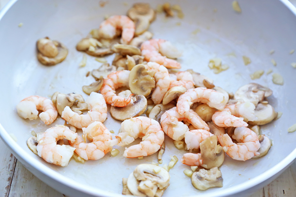 Pink cooked shrimp and browned mushroom slices frying in a white skillet