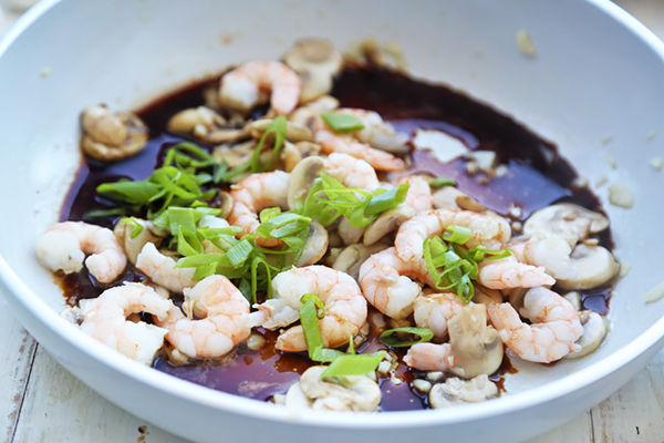 Soy sauce and sliced green onions poured over cooked shrimp and mushrooms in the pan
