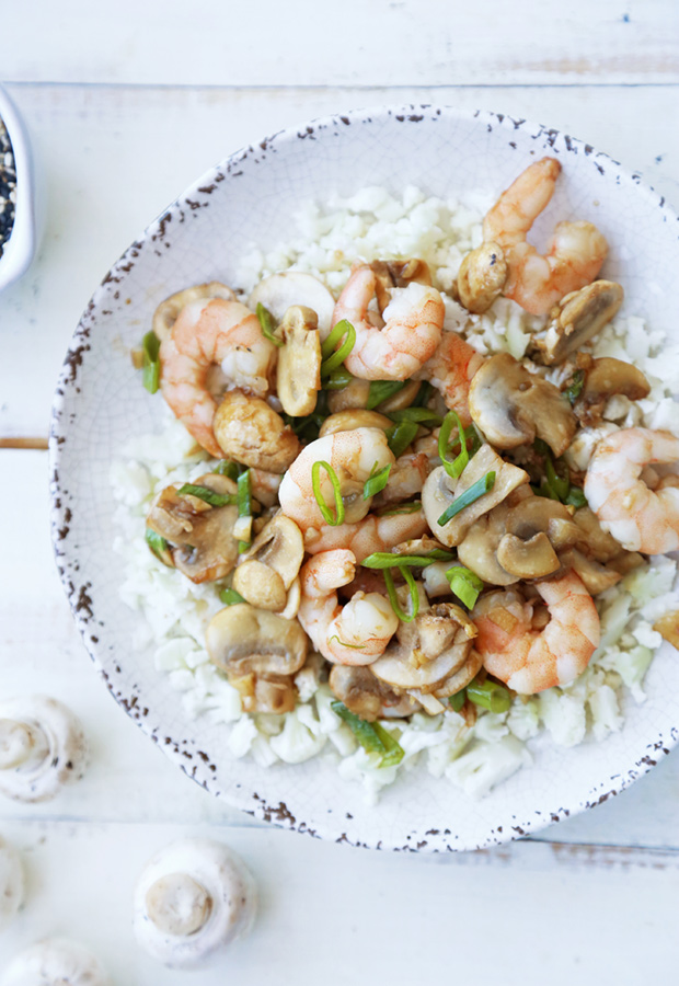 Shrimp and mushroom stir-fry with green onions served over cauliflower rice in a speckled bowl