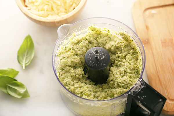 Broccoli and almond flour crust dough pulsed in a food processor with shredded mozzarella nearby