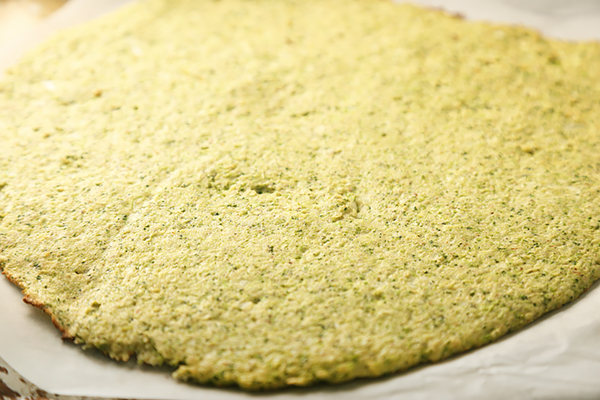 Broccoli pizza crust rolled flat on parchment paper with browned edges