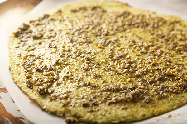 Pesto spread over the baked broccoli crust with crumbled feta scattered on top