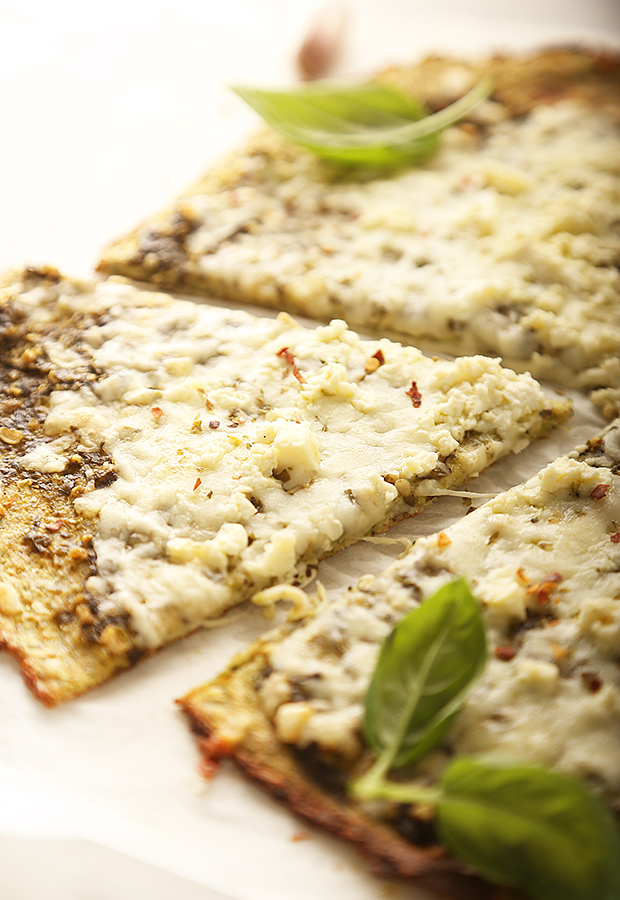 Sliced pesto pizza with melted mozzarella, crumbled feta, and fresh basil leaves