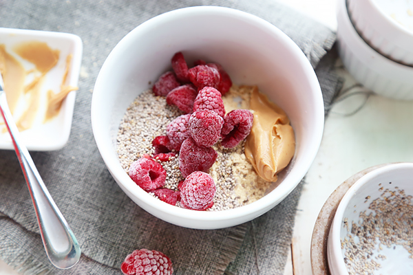 Soaked chia seeds, peanut butter, powdered peanut butter, and frozen raspberries in a large bowl