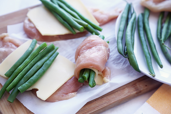 Chicken breast being rolled around swiss cheese and a bundle of green beans