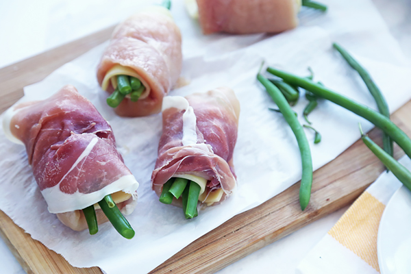Chicken rollups wrapped in prosciutto with green bean ends poking out on a cutting board