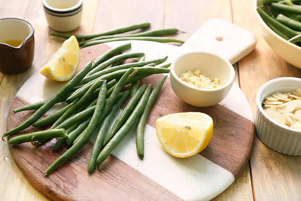 Green beans, lemon wedges, sliced almonds, and minced garlic on a wooden board