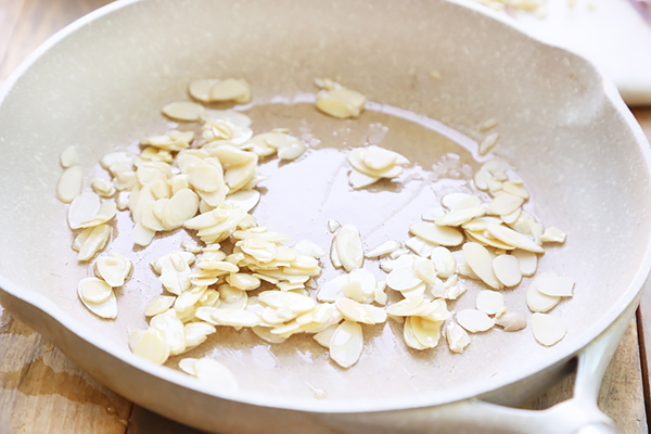 Sliced almonds toasting in olive oil in a light-colored skillet