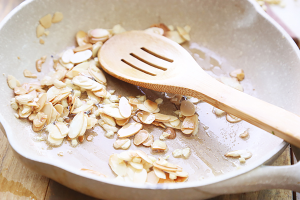 Toasted sliced almonds and garlic browning in a skillet with a wooden spoon