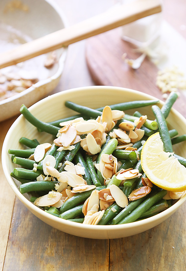 Steamed green beans tossed with toasted almonds and a lemon wedge in a serving bowl