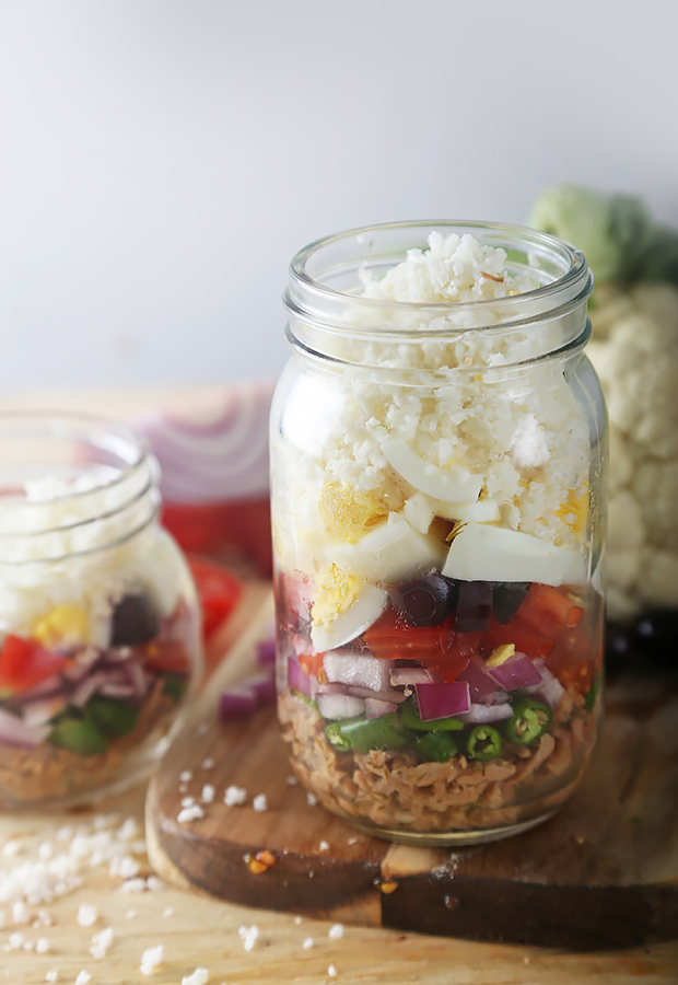 Layered nicoise salad in a mason jar with tuna, vegetables, egg, and cauliflower rice on top