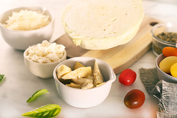 Artichoke hearts, feta, shredded parmesan, cherry tomatoes, and cabbage gathered on a counter